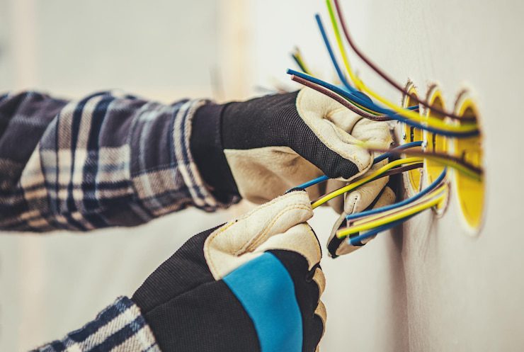 Electrician's gloved hands wiring wall outlet